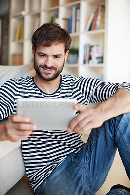 Buy stock photo Shot of a handsome young man using a digital tablet while sitting on the floor at home