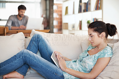 Buy stock photo Shot of an attractive young woman using her digital tablet while reclining on the sofa at home