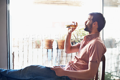 Buy stock photo Shot of a handsome young man drinking a beer while sitting with his digital tablet indoors