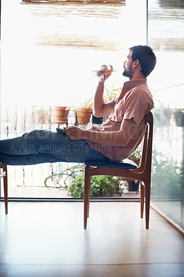 Buy stock photo Shot of a handsome young man drinking a beer while sitting with his digital tablet indoors