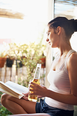 Buy stock photo Shot of an attractive young woman having a beer while reading a book