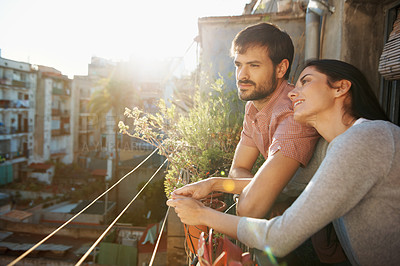 Buy stock photo Shot of a beautiful young couple standing next to each other on a balcony overlooking an urban setting