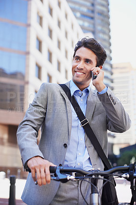 Buy stock photo A handsome businessman talking on his mobile while standing with his bicycle in the city central