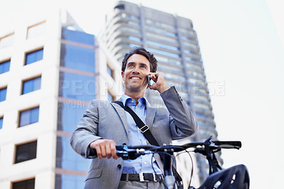 Buy stock photo A handsome businessman talking on his mobile while standing with his bicycle in the city central