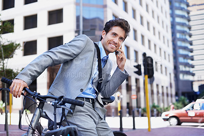 Buy stock photo A handsome businessman talking on his mobile while sitting on his bicycle in the city central
