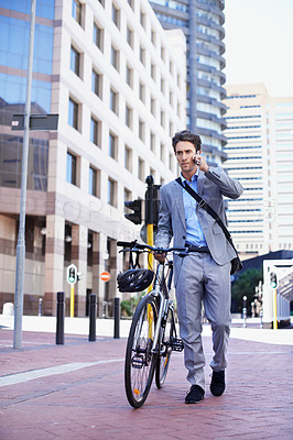 Buy stock photo A handsome businessman talking on his mobile while pushing his bicycle in the city central