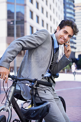 Buy stock photo A handsome businessman talking on his mobile while sitting on his bicycle in the city central