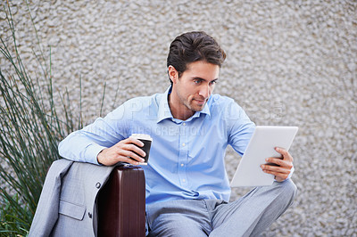 Buy stock photo A handsome businessman using his tablet while sitting out in the city central and having a break