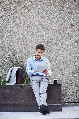 Buy stock photo A handsome businessman using his tablet while sitting out in the city central and having a break