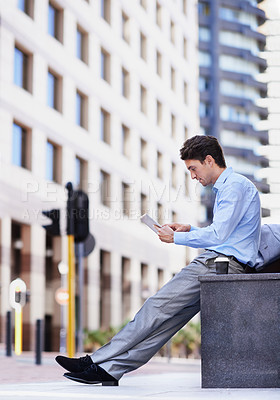 Buy stock photo A handsome businessman using his tablet while sitting out in the city central and having a break
