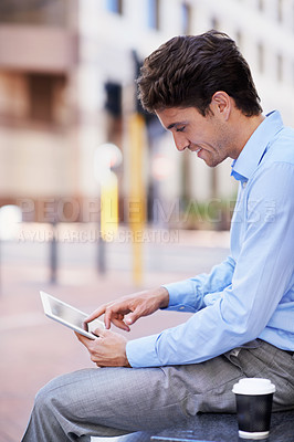 Buy stock photo A handsome businessman using his tablet while sitting out in the city central and having a break