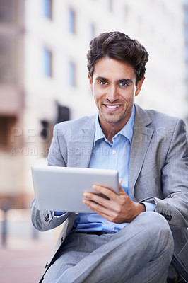 Buy stock photo A handsome businessman using his tablet while sitting out in the city central and having a break