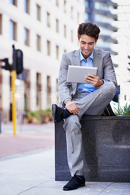 Buy stock photo A handsome businessman using his tablet while sitting out in the city central and having a break