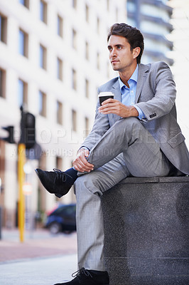Buy stock photo A handsome businessman having a cup of coffee while relaxing in the city
