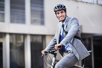 Buy stock photo A handsome businessman riding his bicycle to work in the city central while wearing a bicycle helmet