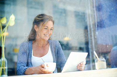 Buy stock photo A woman at a coffee shop sitting by the window smiling and looking at her touchscreen