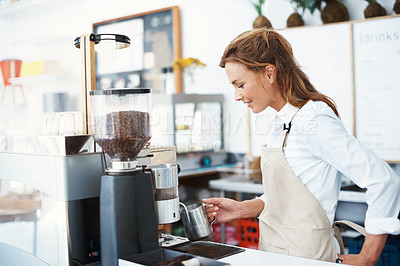 Buy stock photo A pretty barista frothing some milk in the coffee machine beside her