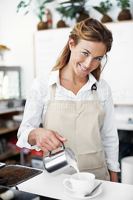 Buy stock photo Portrait of a pretty barista pouring frothed milk into a coffee cup