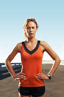 Buy stock photo Female athlete looking at the camera while standing on a highway with her hands on her hips