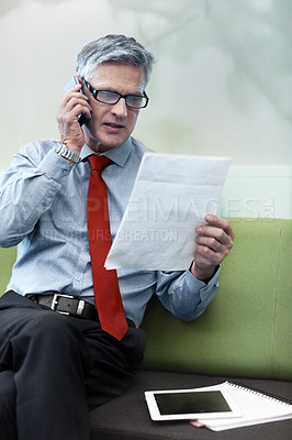 Buy stock photo Shot of a senior businessman reading a document while on the phone