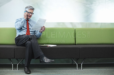 Buy stock photo Shot of a senior businessman reading a document while on the phone