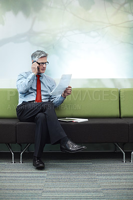 Buy stock photo Shot of a senior businessman reading a document while on the phone