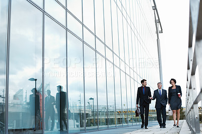 Buy stock photo Shot of three businesspeople walking and talking next to an office building
