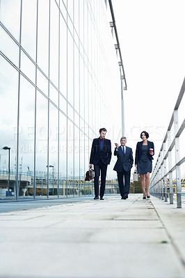 Buy stock photo Shot of three businesspeople walking and talking next to an office building