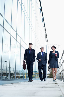 Buy stock photo Shot of three businesspeople walking and talking next to an office building