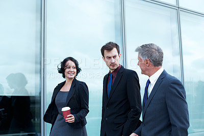 Buy stock photo Shot of three businesspeople walking and talking next to an office building