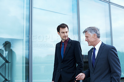 Buy stock photo Shot of two businessmen walking and talking next to an office building
