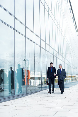 Buy stock photo Shot of two businessmen walking and talking next to an office building