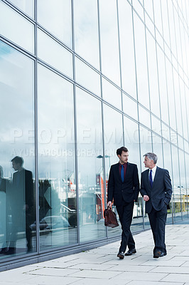Buy stock photo Shot of two businessmen walking and talking next to an office building