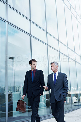Buy stock photo Shot of two businessmen walking and talking next to an office building