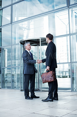 Buy stock photo Shot of two businessmen shaking hands at the entrance of a building