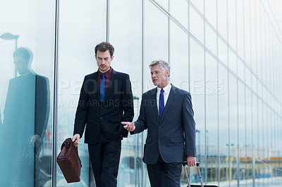 Buy stock photo Shot of two businessmen walking and talking next to an office building