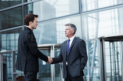Buy stock photo Shot of two businessmen shaking hands at the entrance of a building