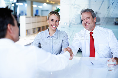 Buy stock photo Shot of two businesspeople shaking hands while sitting in an office