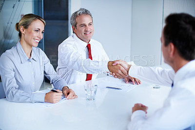 Buy stock photo Shot of two businesspeople shaking hands while sitting in an office