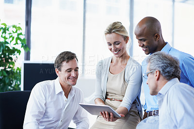 Buy stock photo Shot of a diverse group of businesspeople looking at a digital tablet while standing in an office