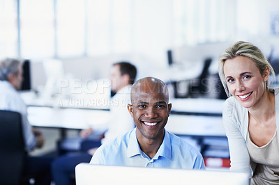 Buy stock photo Portrait of two office workers talking over a desktop computer in an office iwth colleagues in the background