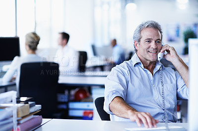 Buy stock photo Shot of a mature businessman talking on a phone while sitting at his desk in an office