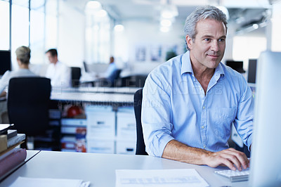 Buy stock photo Shot of a mature businessman working on a computer while sitting at his desk in an office