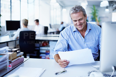 Buy stock photo Shot of a mature businessman looking over paperwork while sitting at his desk in an office