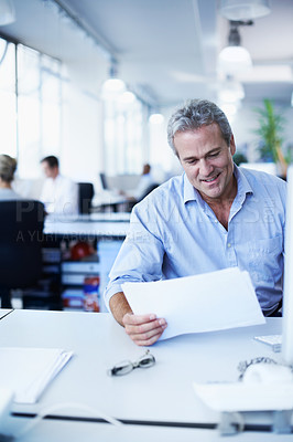 Buy stock photo Shot of a mature businessman looking over paperwork while sitting at his desk in an office