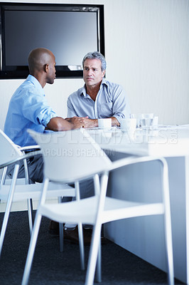 Buy stock photo Shot of two businessman talking while sitting at a boardroom table