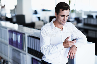 Buy stock photo Shot of a man using a cellphone while standing in an office