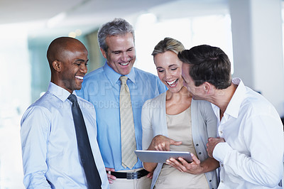 Buy stock photo Shot of a diverse group of coworkers looking at a digital tablet while standing in an office
