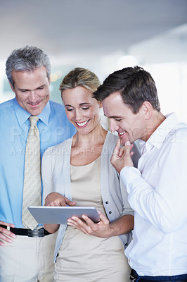 Buy stock photo Shot of a group of coworkers looking at a digital tablet while standing in an office