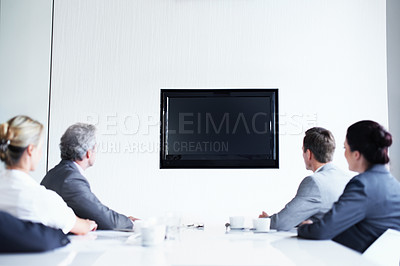 Buy stock photo Rearview shot of a group of businesspeople sitting around a boardroom table looking at a blank monitor